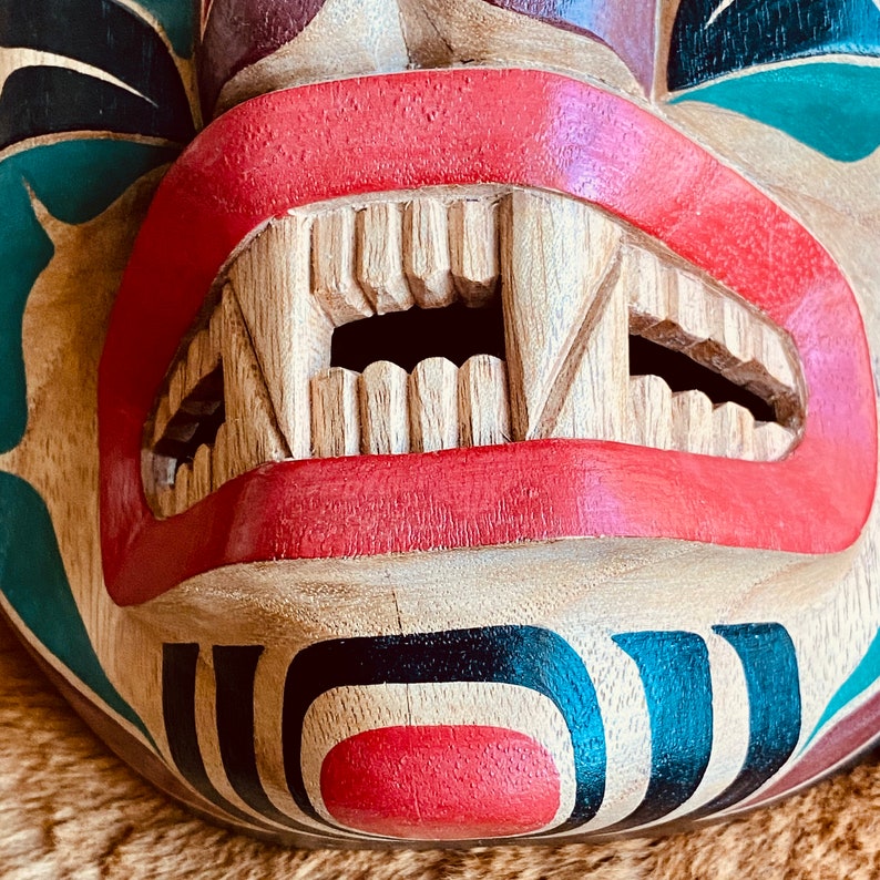 May include: A wooden mask with a carved mouth and teeth, painted in red, black, and green. The mask has a traditional design with geometric patterns.