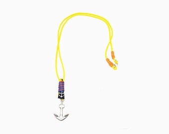 Puede incluir: Un collar de cuerda amarilla con un colgante de ancla de plata. El ancla tiene una banda azul y roja a rayas alrededor de la parte superior.