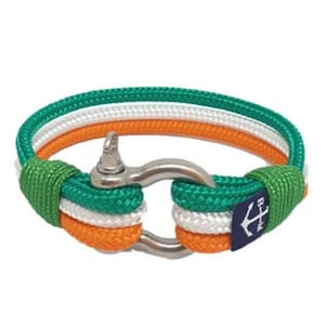 May include: A green, white, and orange rope bracelet with a silver anchor clasp. The bracelet is made of three strands of rope, and the clasp is a simple, round anchor.