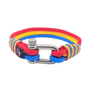 May include: A colorful bracelet featuring red, yellow, and blue rope with a stainless steel clasp. The bracelet has a nautical theme, with a small navy blue tag with a white anchor symbol.