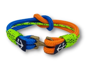 Puede incluir: Un brazalete de cuerda azul y naranja con un acento verde y un cierre de ancla. El brazalete está hecho de dos hebras de cuerda que están anudadas juntas.