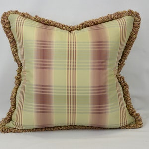 May include: Square decorative pillow with a plaid pattern in shades of green, pink, and cream. The pillow has a ruffled trim in a complementary color. A classic accent piece for a sofa or bed.