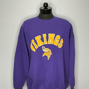 Könnte beinhalten: Lilafarbener Pullover mit einem gelben "VIKINGS"-Logo und einer Grafik eines Wikingerhelms.