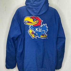 May include: A blue hooded jacket with a large embroidered Kansas Jayhawks logo on the back. The logo features a yellow and red bird with the letters "KU" on its chest.