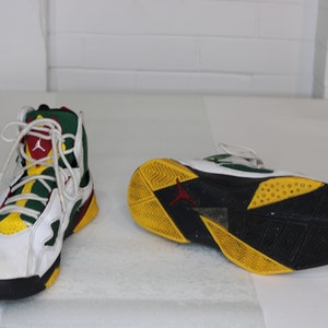 Puede incluir: Zapatillas blancas, verdes, amarillas y rojas de ca&ntilde;a alta con detalles negros. Las zapatillas tienen una suela negra con detalles amarillos y verdes.