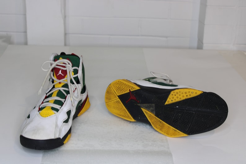 Puede incluir: Zapatillas blancas, verdes, amarillas y rojas de ca&ntilde;a alta con detalles negros. Las zapatillas tienen una suela negra con detalles amarillos y verdes.