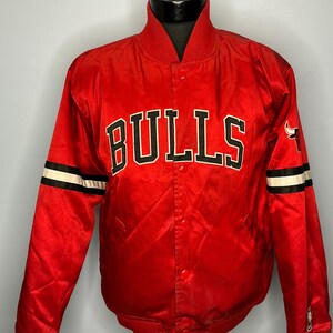 May include: Red satin jacket with the word "BULLS" in black and white block letters across the chest. The jacket has black and white stripes on the sleeves and a Bulls logo on the right chest.