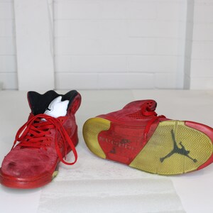 May include: A pair of red suede high-top trainers with black accents and a yellow sole. The trainers have a visible Air Jordan logo on the sole.