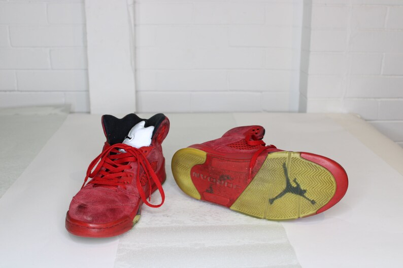 May include: A pair of red suede high-top trainers with black accents and a yellow sole. The trainers have a visible Air Jordan logo on the sole.