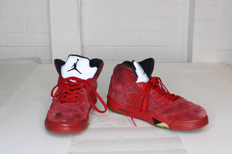 May include: A pair of red suede high-top trainers with black accents and a white Jumpman logo on the side.