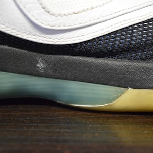 Peut inclure: Gros plan sur la semelle d'une chaussure de sport blanche, noire et bleue avec une semelle verte et jaune.