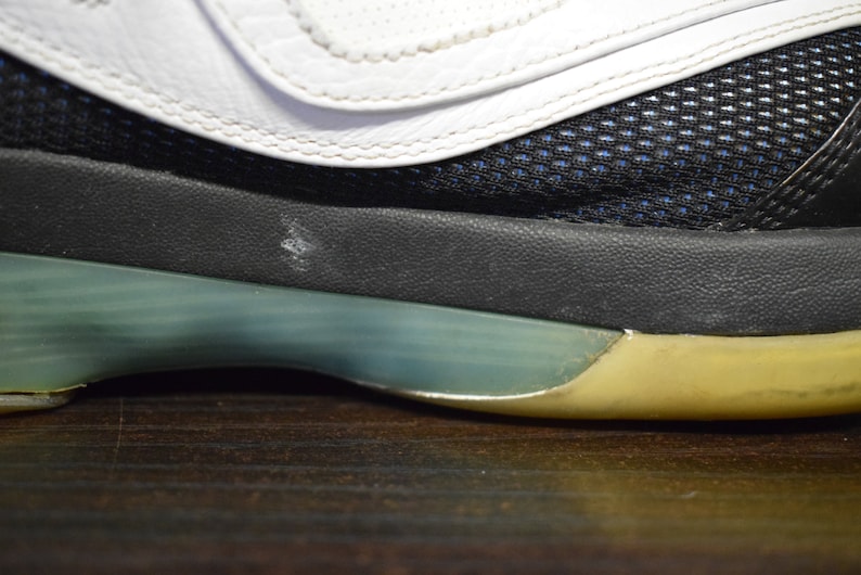 Peut inclure: Gros plan sur la semelle d'une chaussure de sport blanche, noire et bleue avec une semelle verte et jaune.