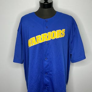 May include: Blue baseball jersey with the word "WARRIORS" in yellow across the chest. The jersey has a button-up front and short sleeves. The fabric has a mesh-like texture.