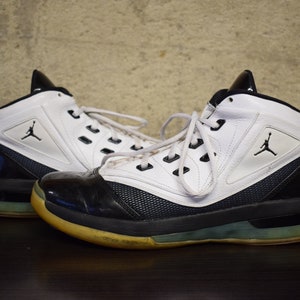 Peut inclure: Une paire de chaussures de basket-ball blanches et noires avec un logo noir et blanc sur le c&ocirc;t&eacute;. Les chaussures ont une semelle noire avec une bande blanche autour du bord.