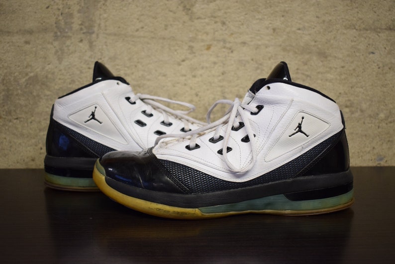 Peut inclure: Une paire de chaussures de basket-ball blanches et noires avec un logo noir et blanc sur le c&ocirc;t&eacute;. Les chaussures ont une semelle noire avec une bande blanche autour du bord.