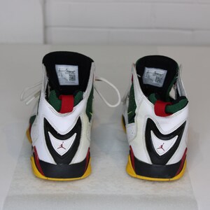 Puede incluir: Un par de zapatillas blancas, negras, verdes, rojas y amarillas de ca&ntilde;a alta con un logotipo Swoosh negro en el lateral.