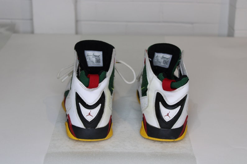 Puede incluir: Un par de zapatillas blancas, negras, verdes, rojas y amarillas de ca&ntilde;a alta con un logotipo Swoosh negro en el lateral.