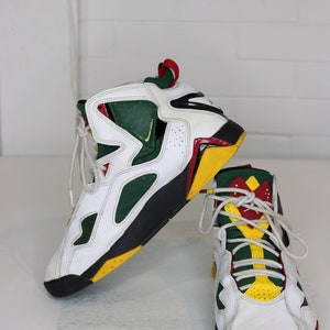 Puede incluir: Un par de zapatillas blancas de ca&ntilde;a alta con detalles en verde, amarillo y rojo. Las zapatillas tienen una suela negra y una parte superior de cuero blanco.