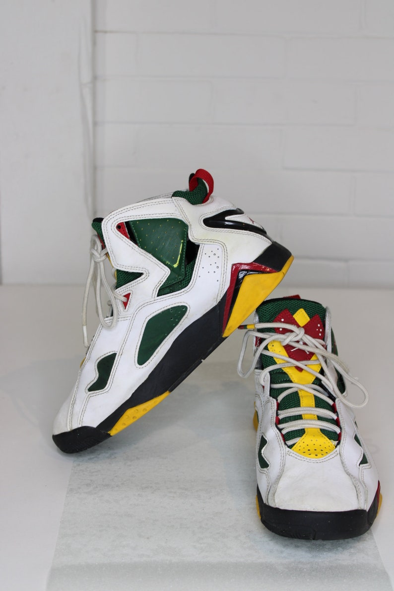 Puede incluir: Un par de zapatillas blancas de ca&ntilde;a alta con detalles en verde, amarillo y rojo. Las zapatillas tienen una suela negra y una parte superior de cuero blanco.