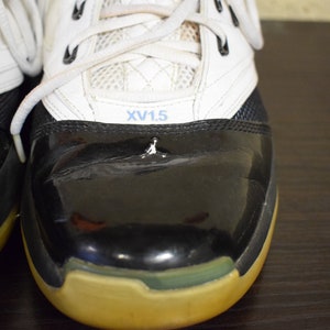 Peut inclure: Une paire de chaussures de basket-ball noires et blanches avec un logo bleu et blanc sur la languette. Les chaussures ont un bout en cuir verni noir et une tige en cuir blanc. Les chaussures sont lac&eacute;es avec des lacets blancs.