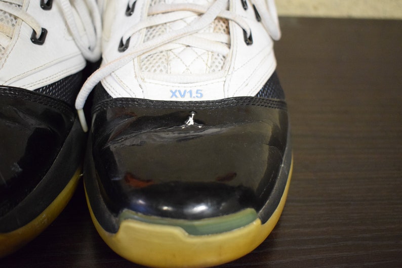 Peut inclure: Une paire de chaussures de basket-ball noires et blanches avec un logo bleu et blanc sur la languette. Les chaussures ont un bout en cuir verni noir et une tige en cuir blanc. Les chaussures sont lac&eacute;es avec des lacets blancs.