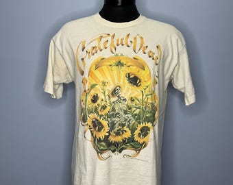 May include: A white t-shirt with a graphic print of a skeleton in a field of sunflowers. The text "Grateful Dead" is written in a stylized font above the graphic.