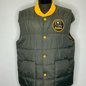 May include: A dark green quilted vest with a yellow collar and yellow buttons. The vest features a Steelers logo patch on the chest. The vest is displayed on a mannequin.