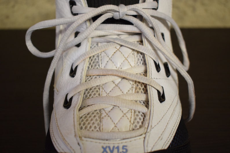 Peut inclure: Gros plan sur des baskets en cuir blanc avec des lacets blancs et des &oelig;illets noirs. Les lacets sont nou&eacute;s en croisillon. La chaussure a un panneau en mesh et un panneau matelass&eacute; blanc. Le texte "XV1.5" est visible sur la chaussure.