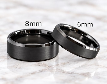 May include: Two black rings with a brushed matte finish and polished beveled edges. One ring is labeled 8mm and the other is labeled 6mm, indicating their respective widths. The rings have a dark, metallic appearance with a smooth, circular band design.