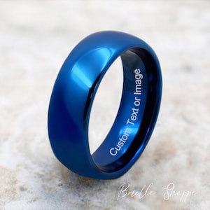May include: A vibrant blue ring with a polished finish. The inner band features the text "Custom Text or Image". The ring is a solid, smooth band, reflecting light. The shop name "Brielle Shoppe" is also visible.