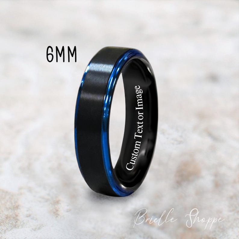 May include: A black tungsten carbide ring with a blue inlay and a custom text inscription. The ring is 6mm wide.