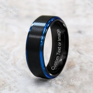 May include: A black tungsten carbide ring with a blue inlay and an inscription that reads "Custom Text or Image".