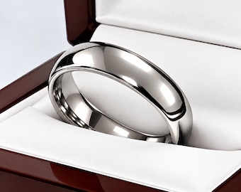 May include: A polished silver-toned metal ring with a smooth, domed surface and a rounded profile. The ring is displayed inside a dark brown wooden presentation box with a white interior lining. The text Brielle Shoppe is visible.