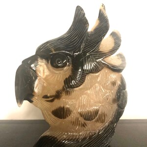 Pode incluir: Uma escultura de p&aacute;ssaro talhada, transl&uacute;cida, de cor castanho claro e preto com um design detalhado. A cabe&ccedil;a do p&aacute;ssaro est&aacute; virada para o lado e seu olho &eacute; vis&iacute;vel.