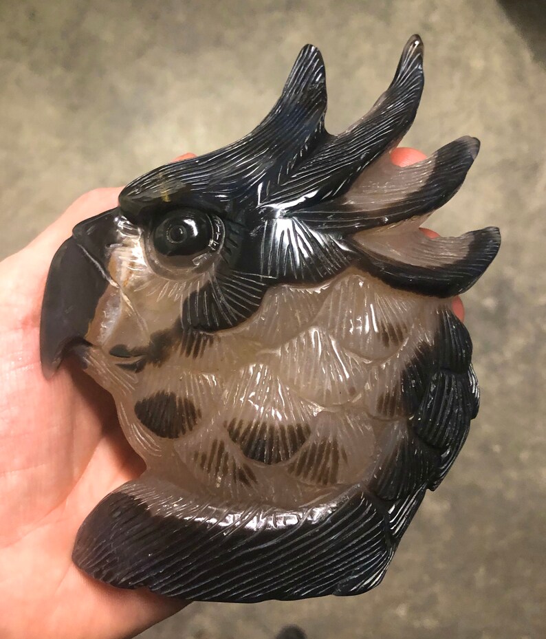 Pode incluir: Uma escultura de &aacute;gata esculpida de uma cabe&ccedil;a de p&aacute;ssaro com marcas pretas e brancas. O p&aacute;ssaro tem uma crista grande e um bico detalhado.