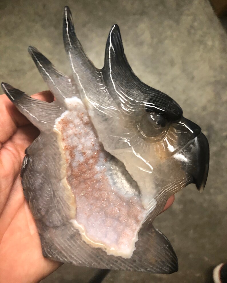 Pode incluir: Uma cabe&ccedil;a de cacatua esculpida em &aacute;gata com um corpo claro e transl&uacute;cido e uma cabe&ccedil;a preta. A &aacute;gata tem uma forma&ccedil;&atilde;o natural, semelhante a um cristal, com uma cavidade oca na parte de tr&aacute;s.