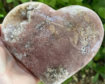 May include: A heart-shaped pink and white agate crystal with a rough, natural texture. The crystal has a light pink hue with white inclusions and a smooth, polished surface.