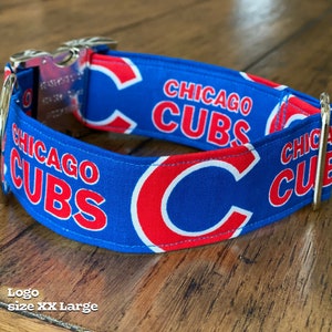 May include: A blue dog collar with the words "CHICAGO CUBS" in red and white. The collar has a metal buckle and D-ring. The size is XX Large.