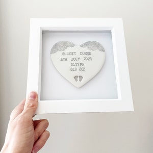 Personalised baby keepsake gift, pearlised white clay heart with lace edge top and baby feet cut out at the bottom of the heart in a white box frame, the heart is personalised with the baby’s name, date of birth, weight and time