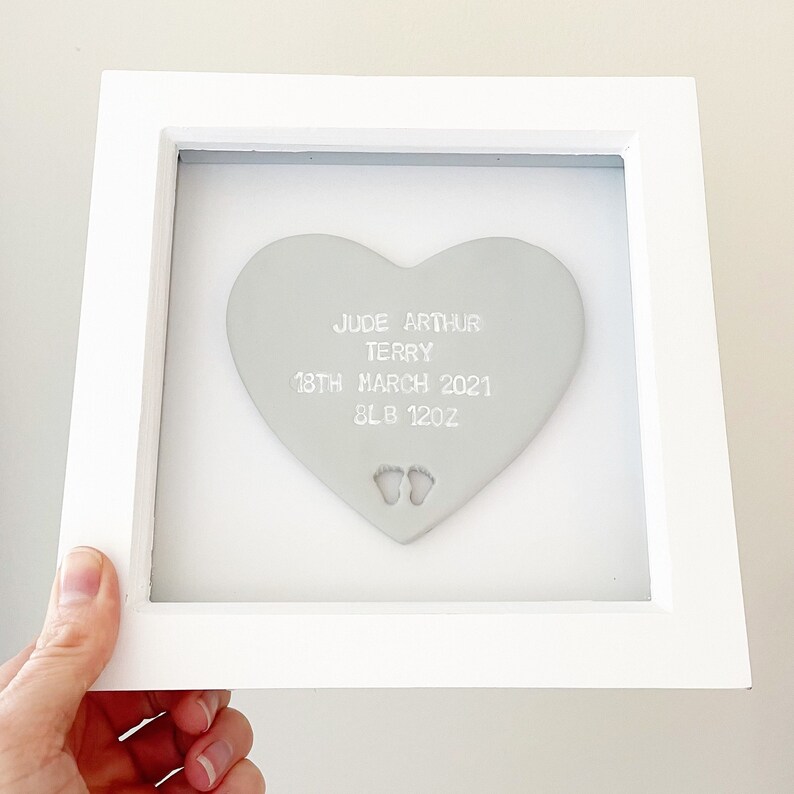 Personalised baby keepsake gift, grey clay heart with baby feet cut out at the bottom of the heart in a white box frame, the heart is personalised with the baby’s name, date of birth, weight and time