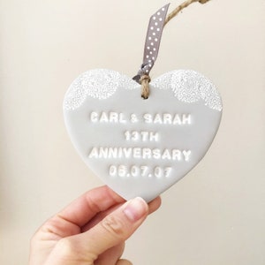 Personalised anniversary gift, grey clay heart with a white lace edge at the top of the heart with jute twine for hanging, the heart is personalised with CARL & SARAH 13TH ANNIVERSARY 06.07.07