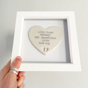 Personalised baby keepsake gift, pearlised white clay heart with baby feet cut out at the bottom of the heart in a white box frame, the heart is personalised with the baby’s name, date of birth, weight and time