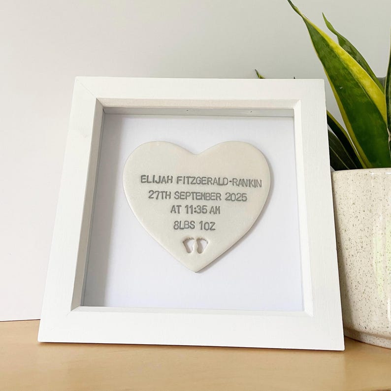 Personalised baby keepsake gift, Pearlised white clay heart with baby feet cut out at the bottom of the heart in a white box frame, the heart is personalised with the baby’s name, date of birth, weight and time