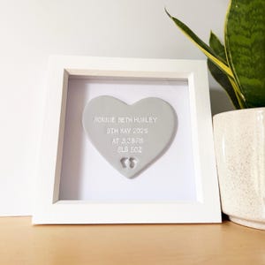 Personalised baby keepsake gift, grey clay heart with baby feet cut out at the bottom of the heart in a white box frame, the heart is personalised with the baby’s name, date of birth, weight and time