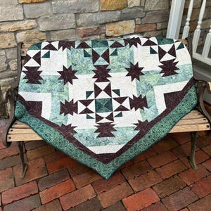 May include: A patchwork quilt featuring a geometric star pattern in shades of dark brown, sage green, and white. The fabric displays a mix of solid colors and marbled textures, finished with a dark green patterned border along the bottom edge.
