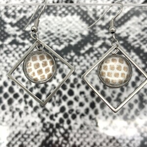 May include: A pair of silver earrings with a square frame and a round, white and brown patterned glass insert.