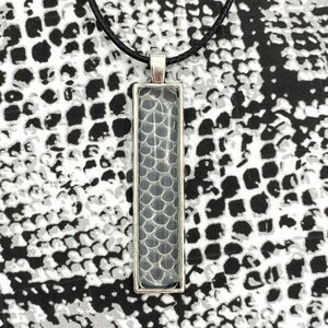 Peut inclure: Un collier avec un pendentif en argent et un charme rectangulaire en verre transparent avec un motif de peau de serpent. Le collier est sur un cordon noir.