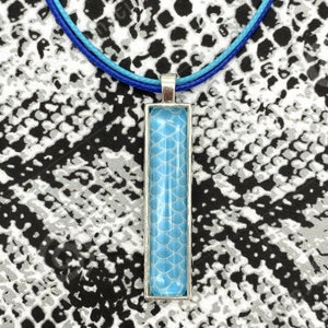 May include: A blue and silver necklace with a rectangular pendant featuring a blue and white scale pattern.