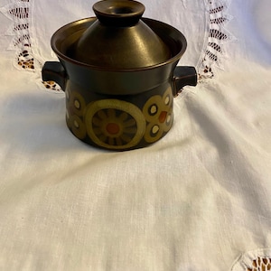 May include: A brown ceramic casserole dish with a lid. The dish features a floral pattern in shades of brown, yellow, orange, and red.