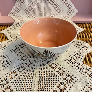 May include: A pink and white ceramic bowl with a floral design. The bowl is sitting on a white crocheted doily.